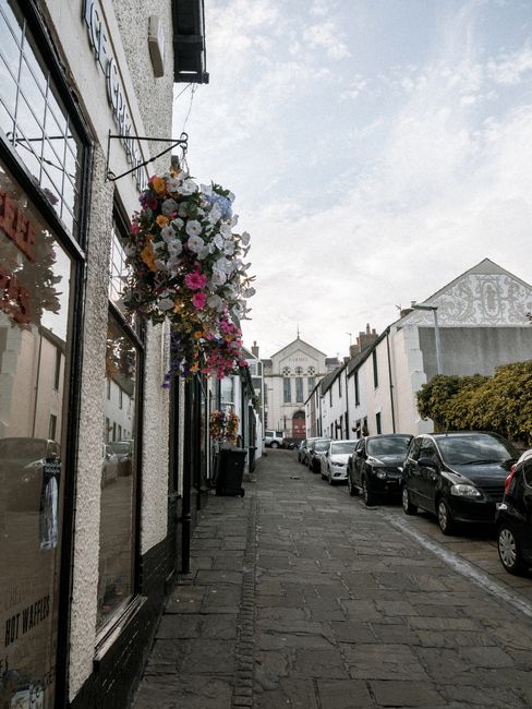 A floral arrangement hanging outside a flower shop on Purfleet High Street. The bouquet features a variety of fresh flowers, including white, pink, yellow, and purple blossoms, arranged in a cascading