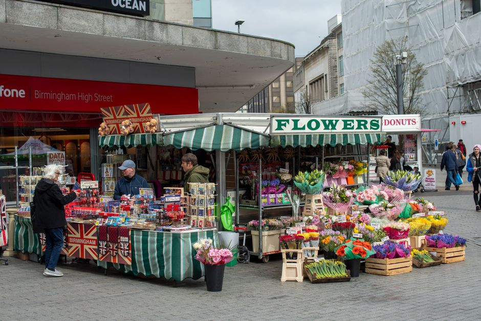 A vibrant outdoor flower stall on Birmingham High Street, operated by flowerspurfleet.co.uk. The stall features a green and white striped canopy sheltering an array of colorful floral arrangements, in